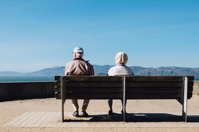 Two old people sitting on a bench and looking at a mountain