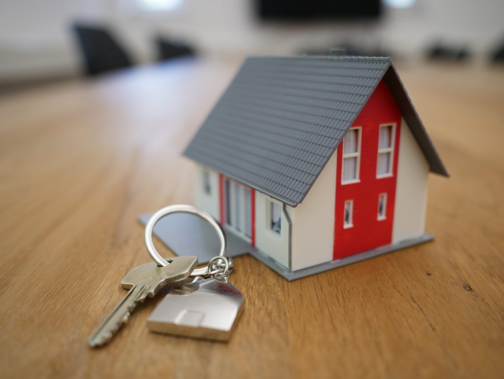 A set of house keys next to a small model house