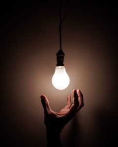 A hand grasping for a lightbulb which is on