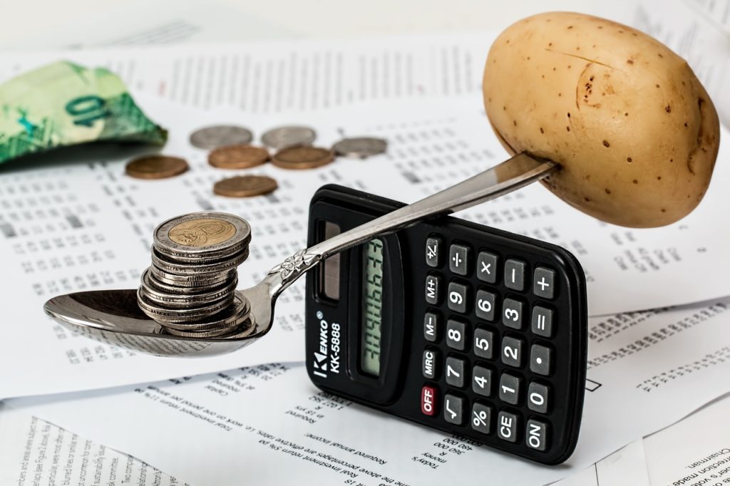 coins balancing on a spoon over calculator counter-balanced with potato